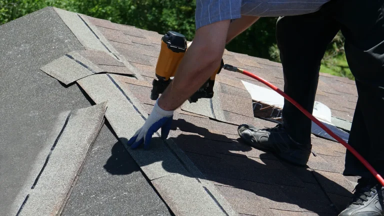 A worker uses a nail gun to attach shingles.